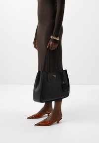 Borsa tote nera con motivo logo in rilievo, finitura opaca e etichetta logo staccabile, abbinata a décolleté marroni a punta.