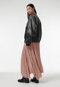 Veste bomber en cuir noir, jupe maxi plissée rose pâle et bottines noires avec des détails en ferraille. Texture lisse et design en couches.