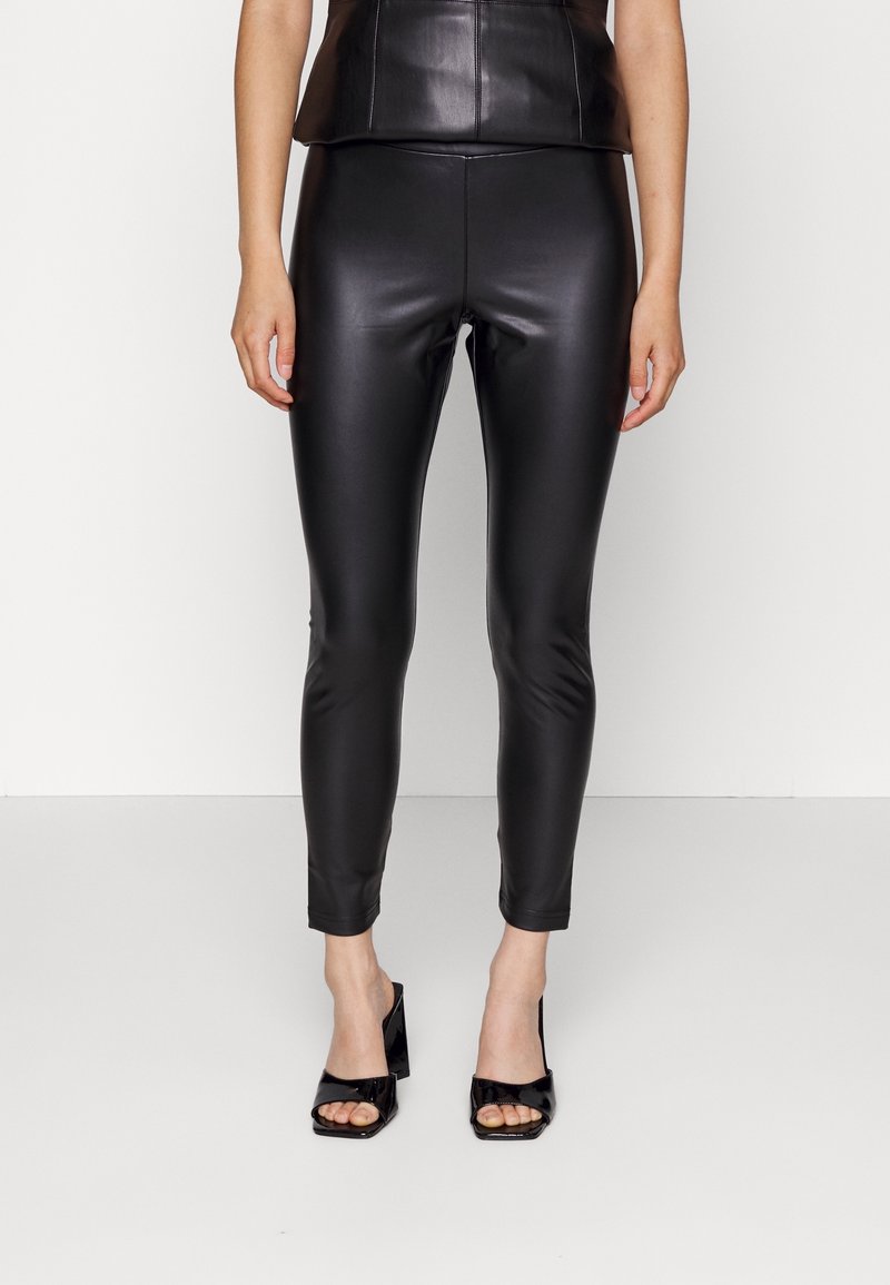 Svarta leggings i konstläder med en åtsittande design, ankellång längd och slät textur, kombinerade med svarta sandaletter med öppen tå och klack.