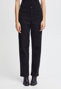 Pantalones de mezclilla negra de pierna recta con bolsillos frontales, cierre de botón y una textura suave. Combinados con botas negras hasta el tobillo.