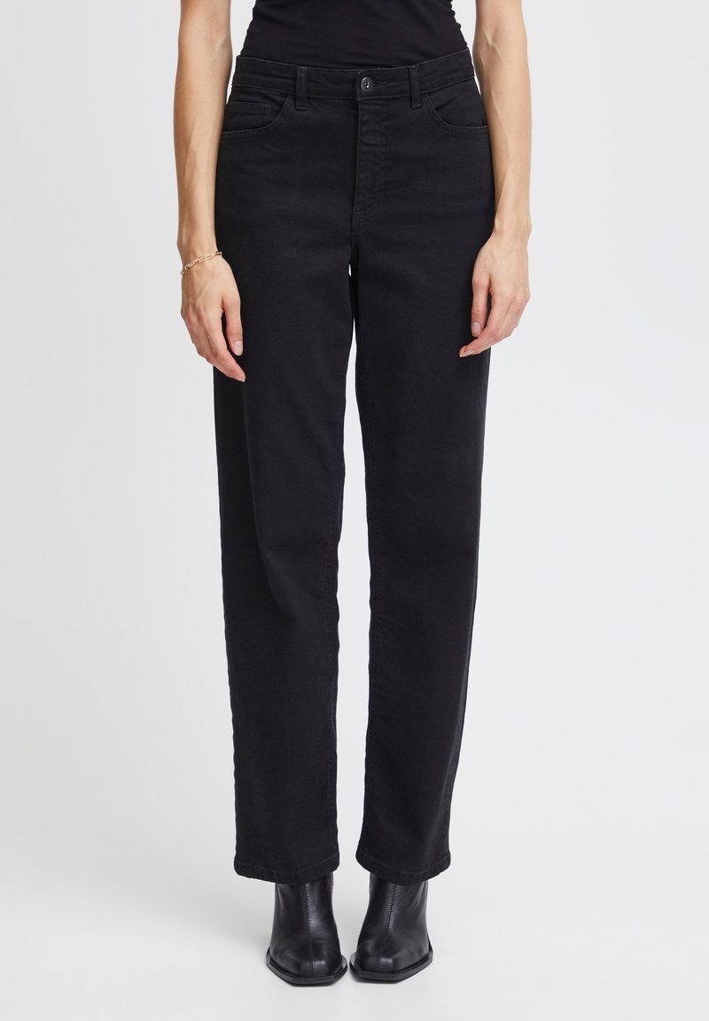 Pantalones de mezclilla negra de pierna recta con bolsillos frontales, cierre de botón y una textura suave. Combinados con botas negras hasta el tobillo.