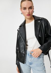 Sort læder bikerjakke med sølvfarvede lynlåse og trykknapper, parret med en hvid t-shirt og lyseblå højtaljede jeans.