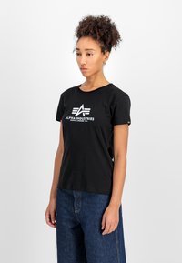 Čierne bavlnené tričko s krátkymi ruk�ávmi, s bielym logom a textovým dizajnom na prednej strane. Kombinované s tmavomodrými širokými džínami.