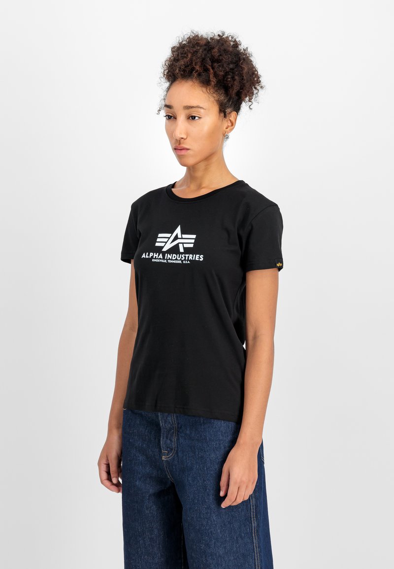 Čierne bavlnené tričko s krátkymi rukávmi, s bielym logom a textovým dizajnom na prednej strane. Kombinované s tmavomodrými širokými džínami.