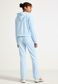 Jasnoniebieska bluza z kapturem i kieszenią kangurką, w komplecie z dopasowanymi jasnoniebieskimi spodniami. Miękka tekstura, dopasowany fason, z widocznymi tylnymi kieszeniami na spodniach.