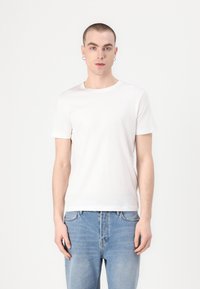 Λευκό βαμβακερό μπλουζάκι με κλασικό στρογγυλό λαιμό, κοντά μανίκια και ομαλή υφή, συνδυασμένο με ανοιχτό μπλε τζιν παντελόνι.