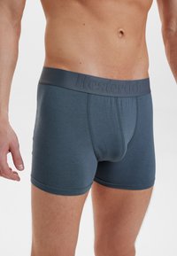 Boxer shorts in dark grey fabric, featuring a smooth texture, a fitted design, and an embossed logo on the waistband.