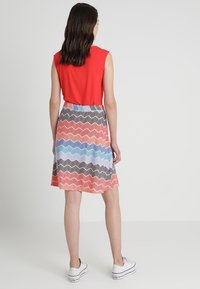 Top rojo sin mangas combinado con una falda de patrón zigzag multicolor en tonos de rosa, azul y negro; usada con zapatillas blancas.