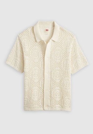 Camiseta de punto de manga corta en color crema con un patrón texturizado de trama abierta y cuello y dobladillo acanalados. Cinco botones en la parte delantera.