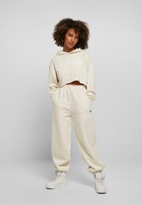 Haut à capuche court couleur crème avec le logo "STARTER", associé à un pantalon de survêtement crème et des baskets montantes blanches, avec une coupe décontractée.