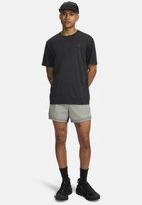 Mustad lühikeste varrukatega särk logoga, helehallid lühikesed püksid tumedama äärega ja mustad jalanõud. Modellil on must müts ja näha on tätoveeringuid.