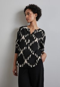 Blusa nera con motivo astratto color crema, scollatura a V, maniche lunghe e bottoni. Realizzata in materiale morbido, vestibilità comoda, orlo leggermente arrotondato.