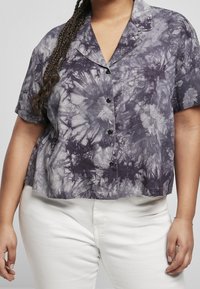 Maglietta corta a maniche corte, tagliata, in un motivo tie-dye di grigio e viola scuro, con chiusura a bottoni e un tessuto morbido e strutturato.