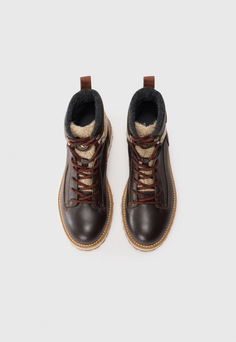 Donkerbruine leren laarzen met beige fleece voering, bruine veters en rubberen zolen. Heeft een gestructureerde buitenkant en contrasterende accenten.