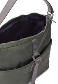 Bolsa de nailon verde con correa ajustable gris, cierre de cremallera y interior negro. Presenta un bolsillo exterior y un detalle del logo de KCB en el lateral.