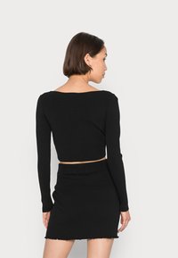 Top crop preto com nervuras, mangas longas e decote largo, combinado com uma saia preta correspondente com uma bainha desfiada.