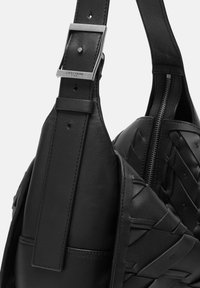 Czarna skórzana torebka na ramię o plecionej fakturze, z metalową klamrą w kolorze srebrnym na pasku i zamknięciem na zamek błyskawiczny. Miękkie wykończenie.