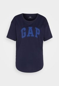 Námořnická modrá bavlněná tričko s výrazným modrým logem "GAP" v zaobleném písmu, krátkými rukávy a zakřiveným lemem pro pohodlný střih.