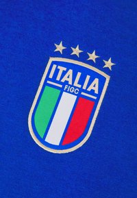 Tessuto blu con un logo scudetto ricamato che presenta quattro stelle, la parola "ITALIA" e i colori della bandiera italiana: verde, bianco e rosso.