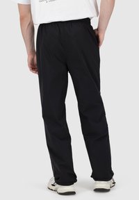 Schwarze, leichte, elastische Hose mit entspannter Passform und geradem Bein; getragen mit einem weißen Grafik-T-Shirt und Sneakers.