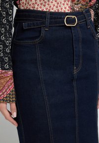 Granatowa spódnica dżinsowa z kontrastowymi przeszyciami, dopasowany krój i pasek z prostokątną złotą klamrą. Posiada kieszenie z przodu.