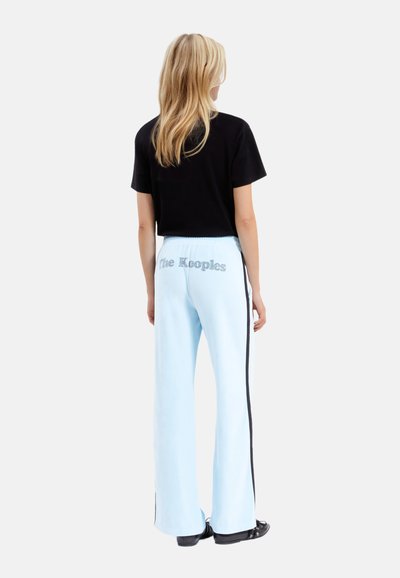 Pantaloni della tuta azzurro chiaro con forma svasata, strisce laterali nere e "The Kooples" ricamato in argento sul retro. T-shirt nera aderente.