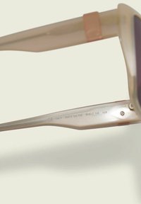 Para półprzezroczystych, jasnoróżowych okularów przeciwsłonecznych z ciemnymi soczewkami, z wąską oprawą i wygrawerowanymi detalami na wewnętrznej części zauszników.