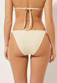 Krämfärgad bikiniunderdel med strukturerad, zick-zack mönster. Knyts på båda sidor, och en slät yta synlig vid kanterna.