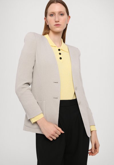 Light gray blazer with a tailored fit, featuring two front buttons, a textured fabric, and two side pockets. Paired with a yellow collared top.