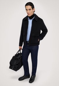 Mörkgrå ullblandningsjacka med två framfickor, bärs över en blårandig skjorta. Mörka jeans och svarta läderskor. Bär en svart väska.