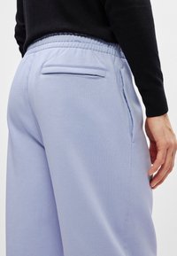 Απαλά μωβ φόρμες φτιαγμένες από μαλακό ύφασμα, με ελαστική μέση και μια μικρή λεπτομέρεια πίσω από την τσέπη, με λεία υφή.