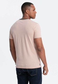 Lyserød kortærmet t-shirt i et blødt, tekstureret stof med en rundt sort krave. Bagfra vises et glat design og et mærke ved sømmen.