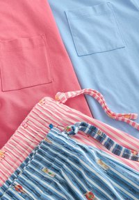 Rosa und blaue Stoffe mit eingenähten quadratischen Taschen über zwei Beuteln mit Kordelzug, ein rosa gestreift und ein blau gestreift mit kleinen Strandabbildungen.