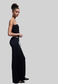 Sort stropløs top med ribbet tekstur kombineret med brede sorte bukser. Sættet har en snor i taljen og elegante flade sko.