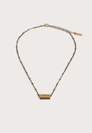 Collier chaîne doré avec petits détails de perles et pendentif rectangulaire gravé du mot "VERSACE" sur fond blanc.