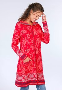 Roter, blumengemusterter langer Mantel mit Kapuze, ausgestattet mit einem Reißverschluss vorne, zwei Taschen und kontrastierenden blauen und weißen Akzenten an den Ärmeln und dem Saum.