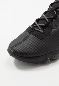 Svart atletisk sko med ett texturerat kviltat mönster, grå snören och en rundad sula med subtila accentuerade delar för grepp.