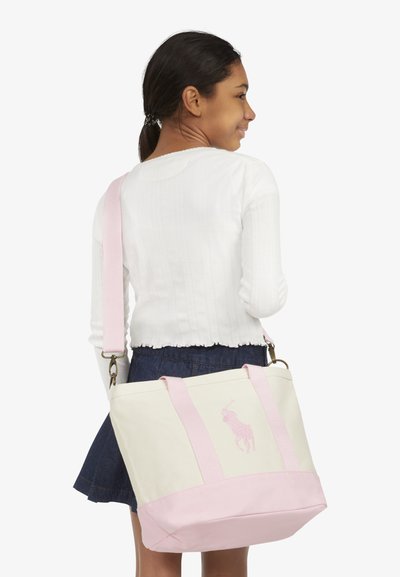 Drobės nešiojimo krepšys su rožinės spalvos pagrindu ir rankenomis, puoštas rožinės spalvos siuvinėtu logotipu. Krepšys yra stačiakampio formos ir tvirtas.