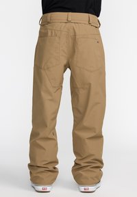 Pantalons cargo marron avec une coupe droite, dotés de deux grandes poches arrière, des passants de ceinture et un ourlet renforcé pour plus de durabilité.