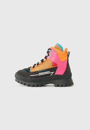 Botte de randonnée colorée présentant un mélange de matériaux noirs, roses, oranges et beiges, avec une semelle épaisse, un col rembourré et une marque distincte.