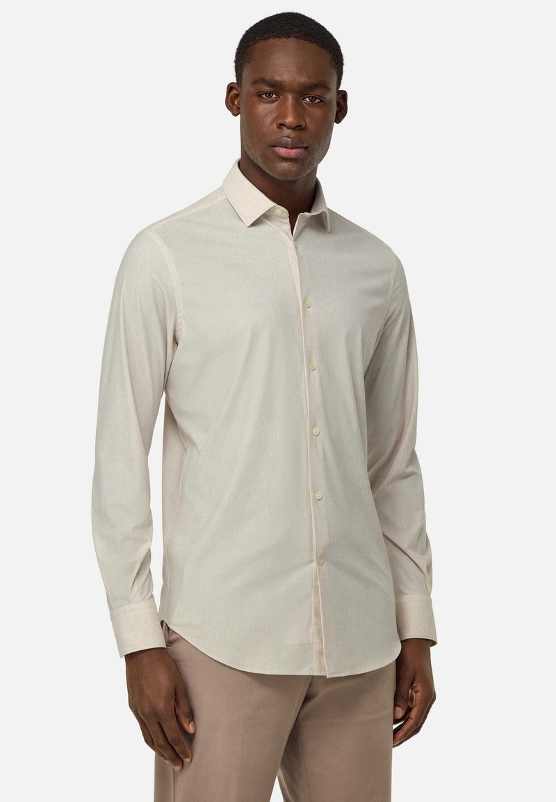 Camisa de manga larga beige clara con cuello abotonado, que presenta una textura de tela suave y un sutil detalle de costura a lo largo de las costuras.