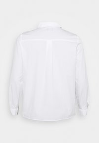 Vit skjorta med klassisk krage, långa ärmar och rak fåll. Baksidan har en diskret sömdetalj för ökad struktur.