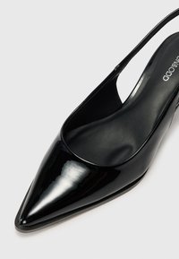 Černé lakované kožené slingback lodičky s špičatou špičkou a hladkým povrchem. Disponují štíhlým designem a nízkými bočními částmi pro moderní vzhled.