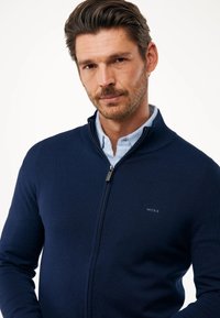 Sudadera navy de cremallera en tejido de punto con cuello alto, logo bordado en el pecho y sutiles puños y dobladillo acanalados.