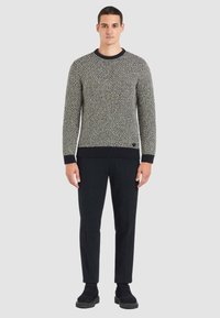 Maglione lavorato a maglia in bianco e nero con trama, collo rotondo, polsini e orlo a costine, abbinato a pantaloni neri e calzature nere.