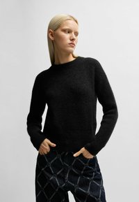Pullover in lana nera con una finitura testurizzata, scollatura a girocollo e maniche lunghe. Abbinato a pantaloni scuri con un motivo a diamante.