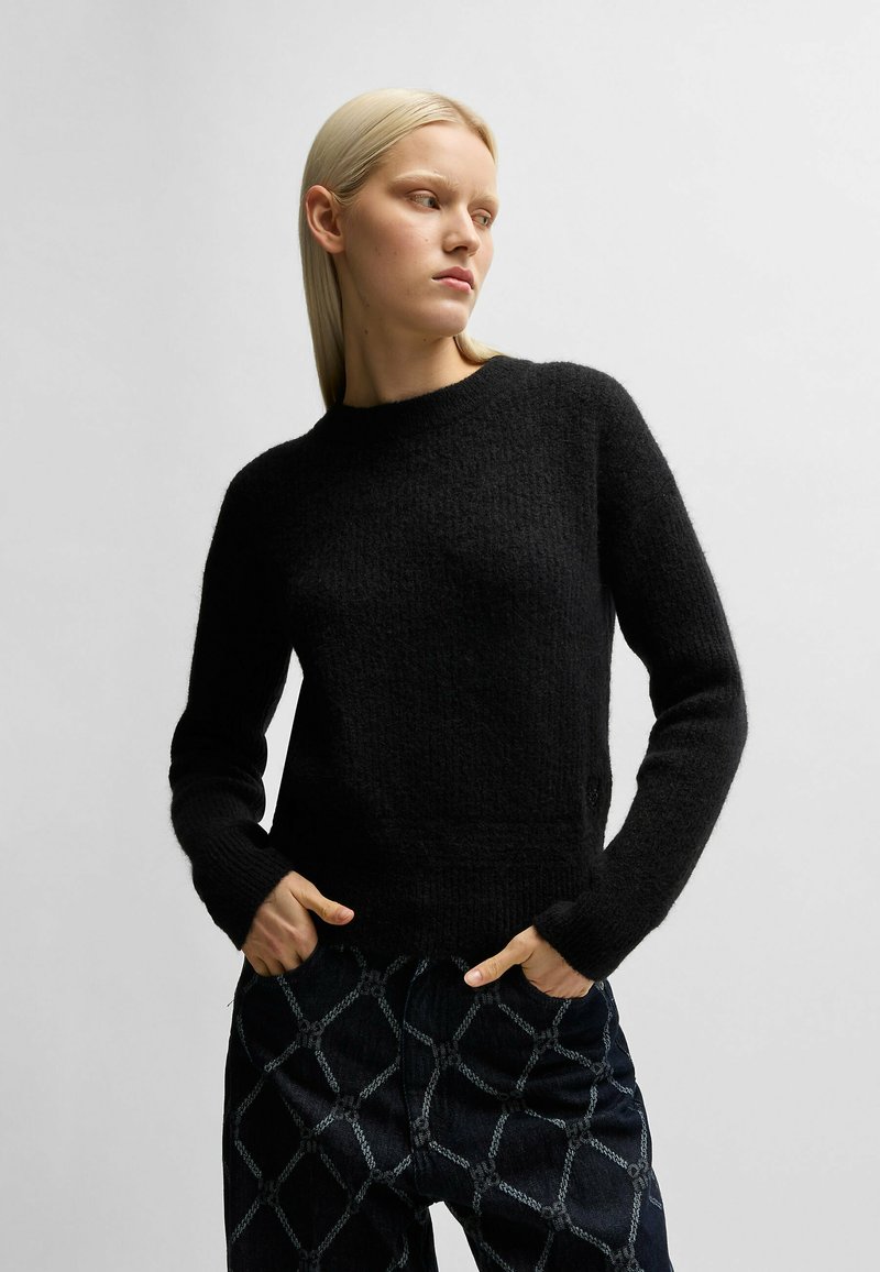 Pullover in lana nera con una finitura testurizzata, scollatura a girocollo e maniche lunghe. Abbinato a pantaloni scuri con un motivo a diamante.