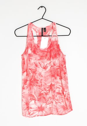 Bezrekawnik w koralowym kolorze z tropikalnym kwiatowym wzorem, wiszący na czarnym wieszaku na białym tle.