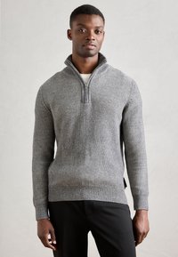 Suéter gris de canalé con cuello de media cremallera, confeccionado en un material de punto texturizado, con mangas largas y una silueta ajustada.