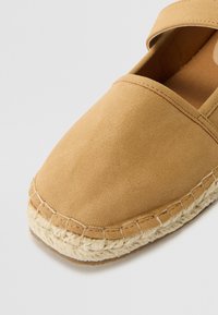 Sandale espadrille en suede beige avec une semelle en jute tressé et des détails cousus. Bout arrondi et bride de cheville pour un soutien. Texture douce.